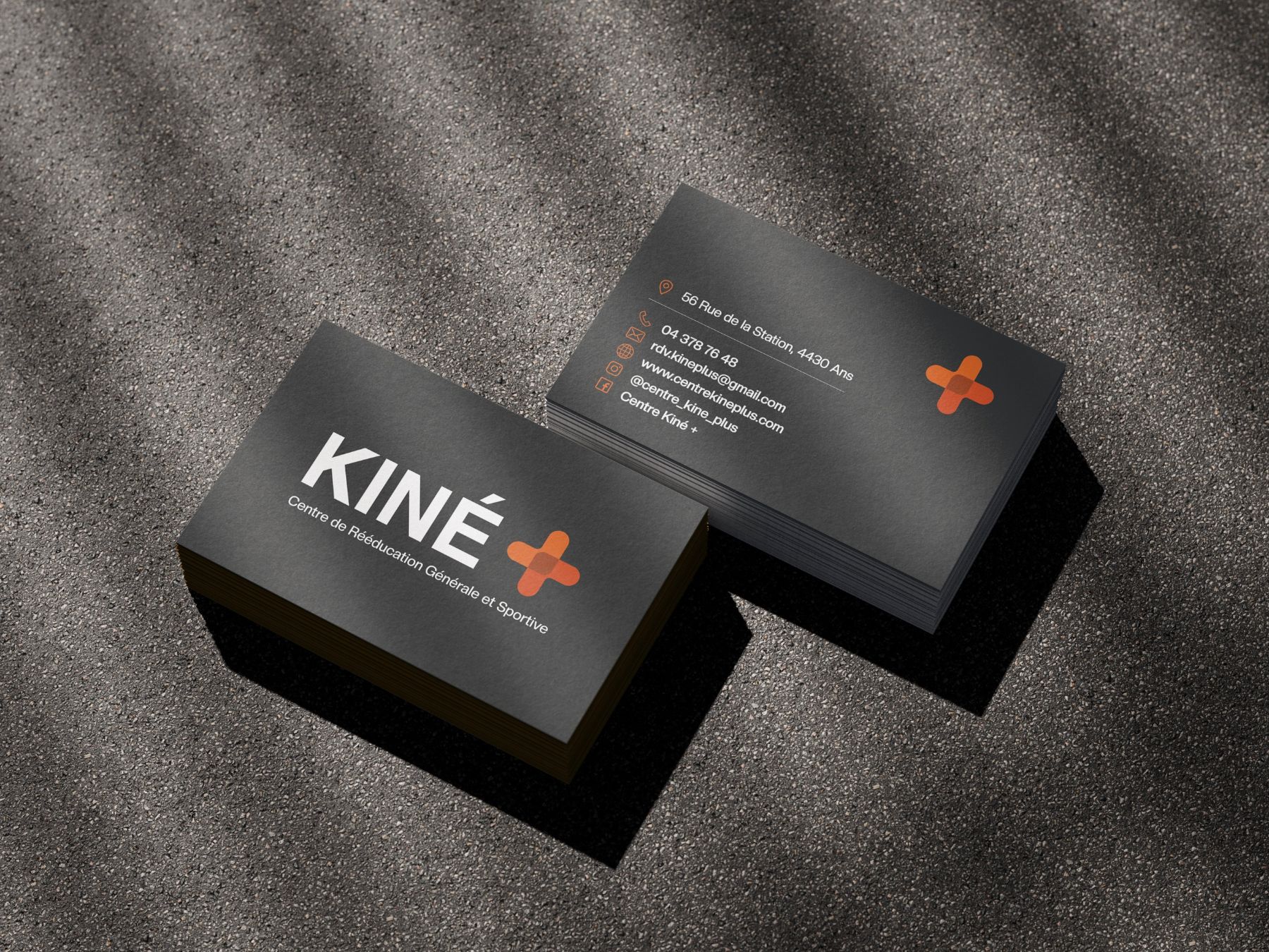 Les cartes de visite KINÉ+ : encre sombre, croix orange, posées sur un fond texturé